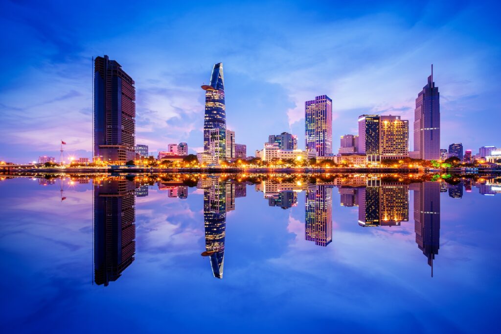 Cityscape In Reflection Of Ho Chi Minh City At Beautiful Twilight, Viewed Over Saigon River. Hochiminh City Is The Largest City In Vietnam With Population Around 10 Million People